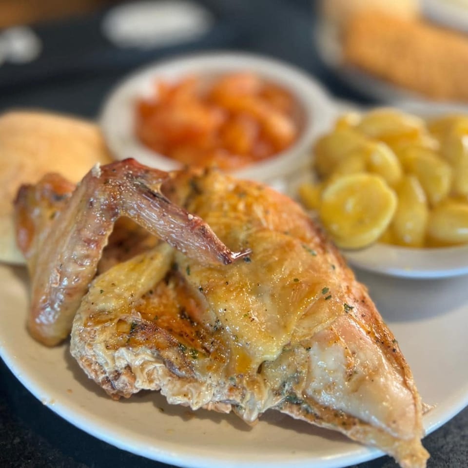 Roasted chicken with a side of macaroni and cheese and diced tomatoes on a white plate.